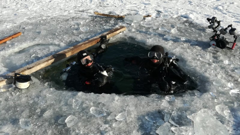 Potápači pri zasneženej diere v jazere